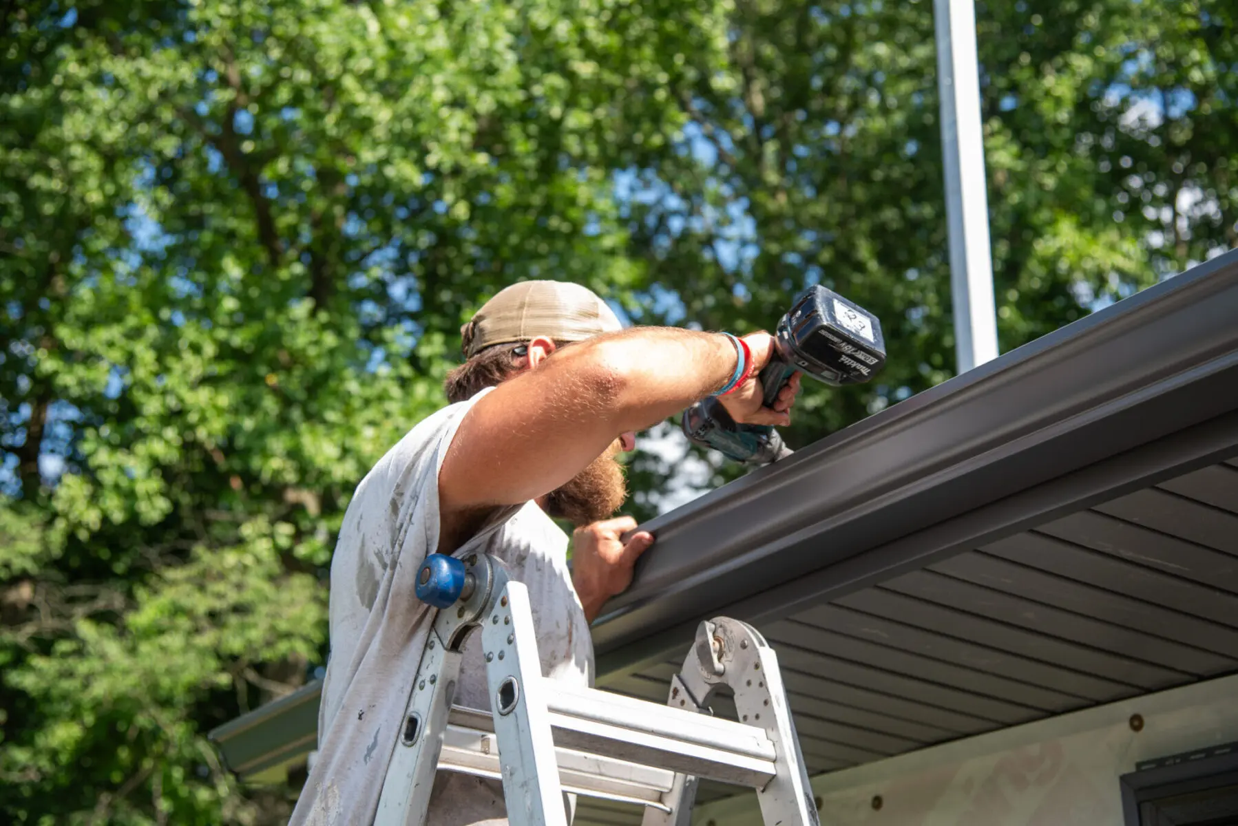 man standing on a ladder working on gutters