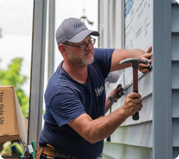 mast roofing and construction employee hammering siding