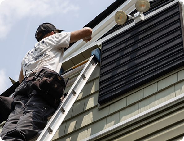 mast roofing and construction employee standing on a ladder working on a roof